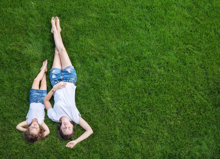 Mother and daughter relaxing on a green freshly mowed lawn with no weeds