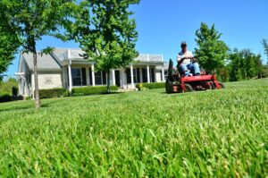 Lawn care employee sitting on a lawn mower in front of residential property in the lawn