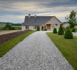 Driveway to a residential home with groomed gravel driveway, freshly mowed lawn and well maintain landscaping